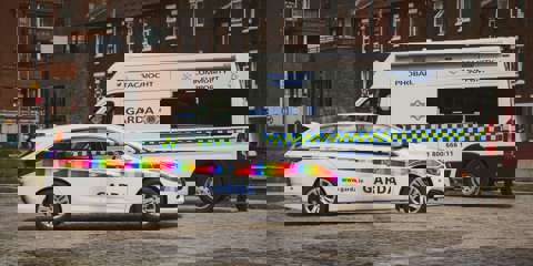 Rainbow flag-branded Garda car and a Garda community support van parked on a cobblestone street.