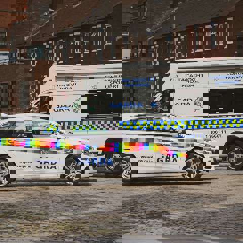 Rainbow flag-branded Garda car and a Garda community support van parked on a cobblestone street.