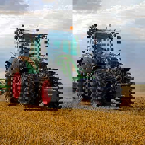 A green tractor is actively harvesting crops in a sunlit field.
