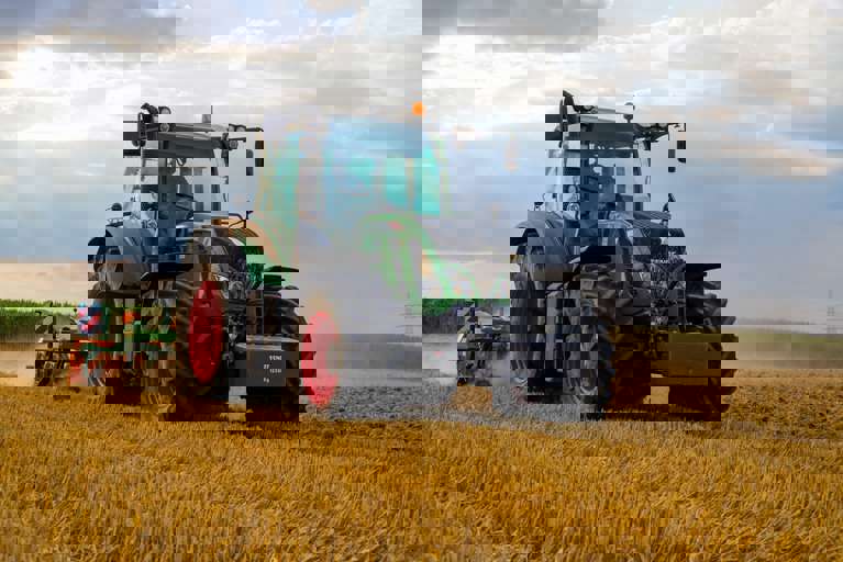 A green tractor is actively harvesting crops in a sunlit field.