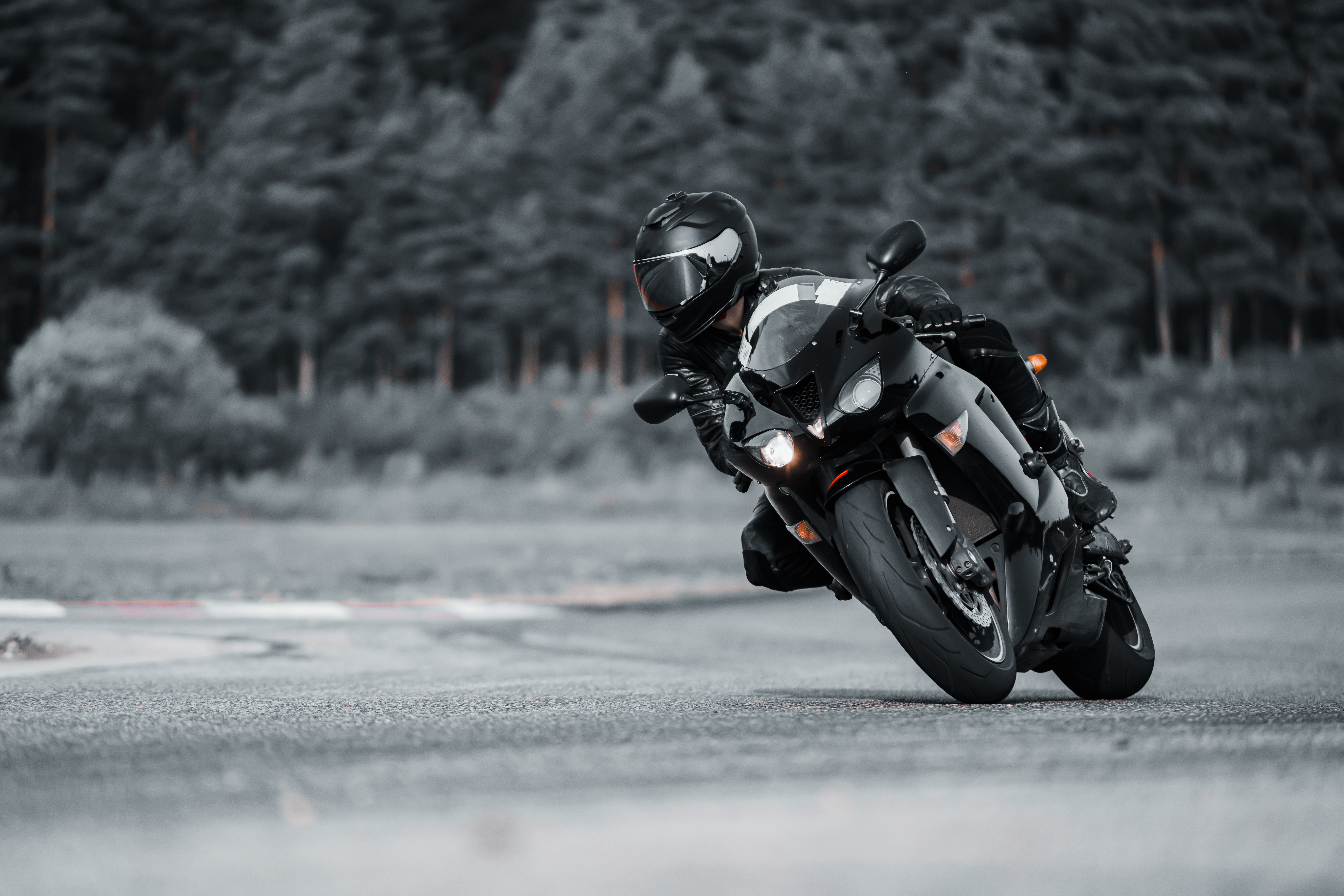 Motorcyclist leaning into a corner on a black sports bike riding on a wet road with a blurred forest background.
