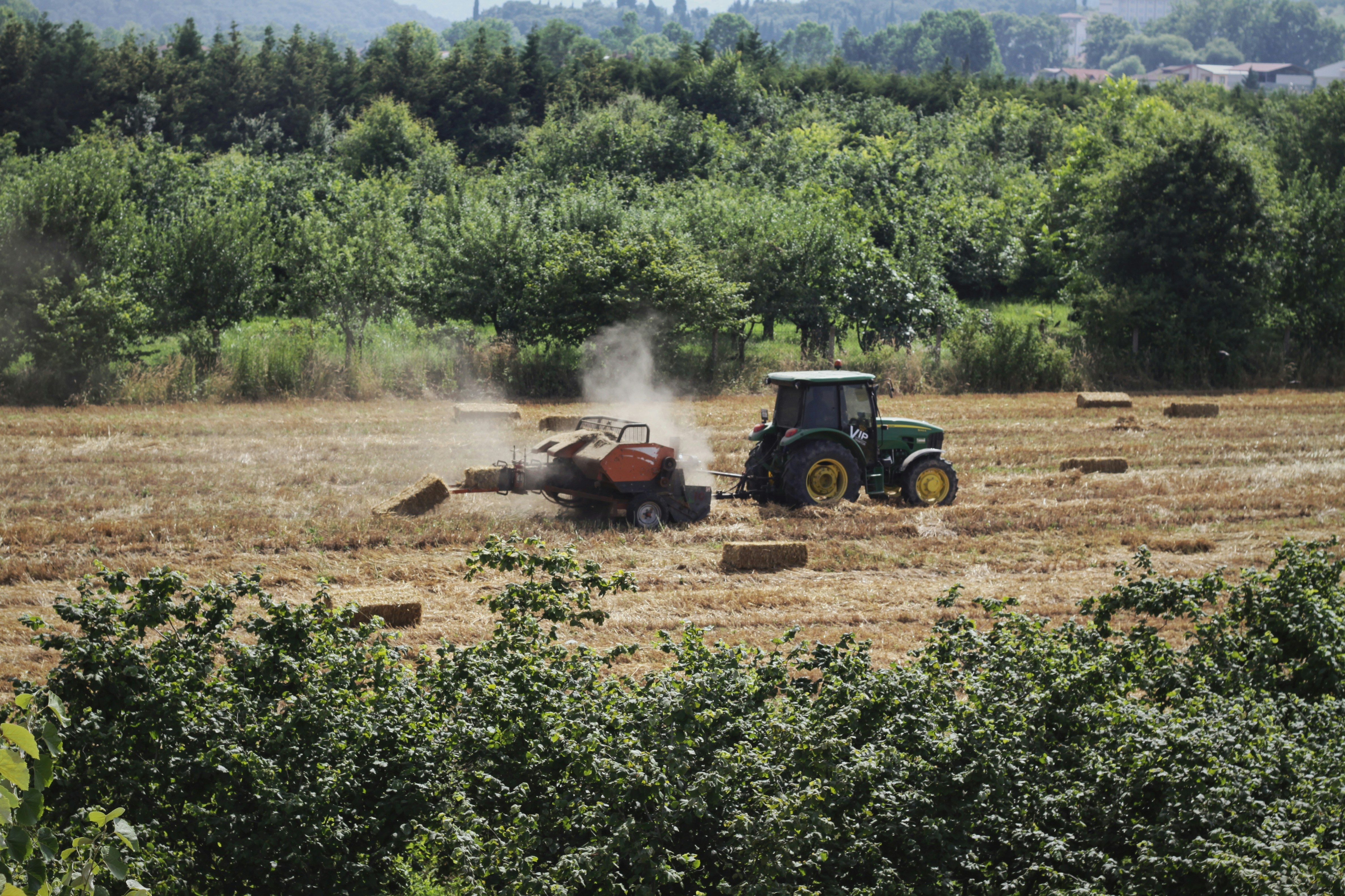 Green tractor at work baling hay in a rural countryside landscape.