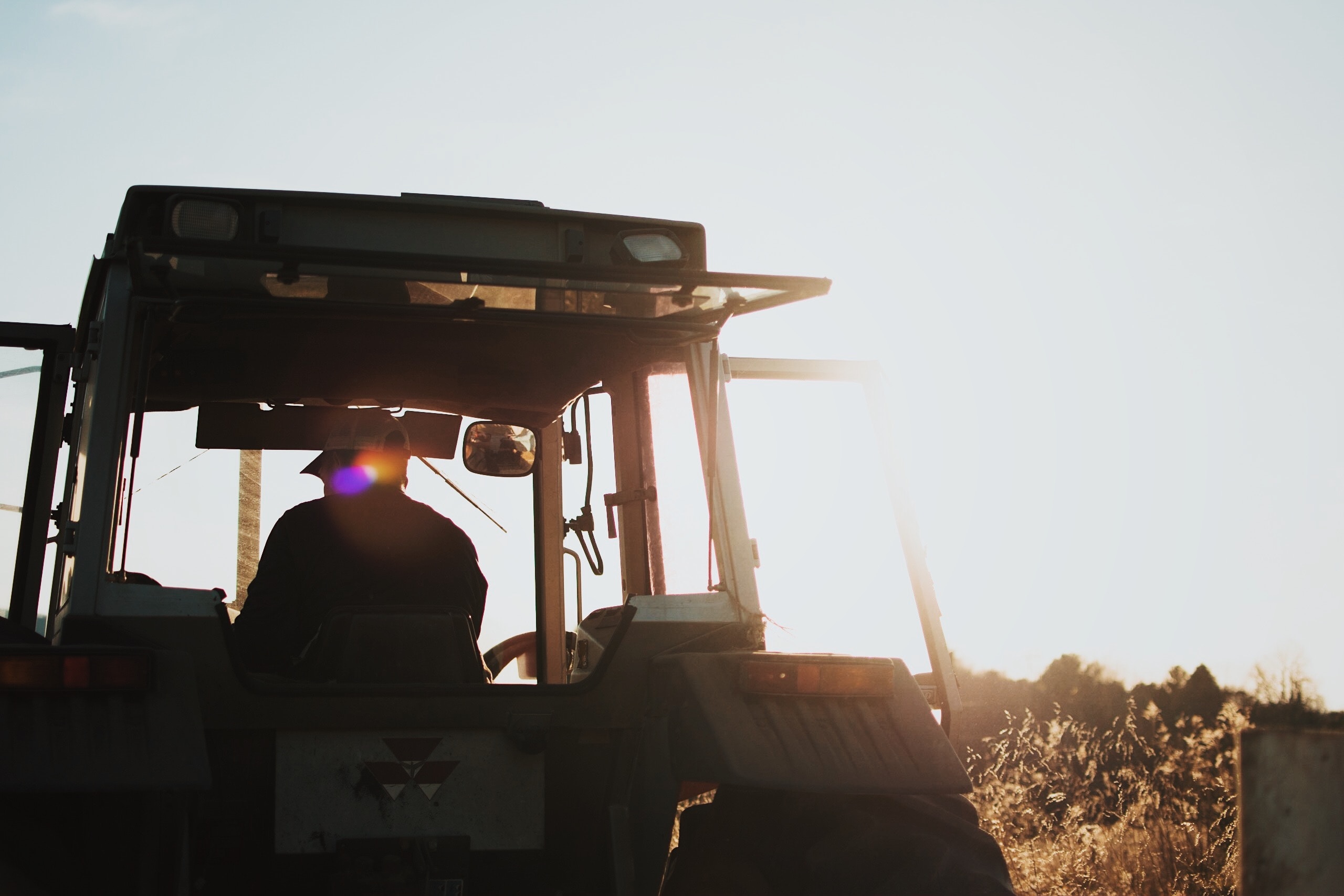 A farmer operates a tractor under clear, sunny skies.