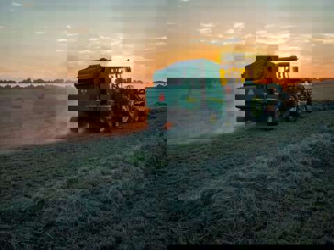 Evening harvest with green tractor and round baler silhouetted against the sunset.