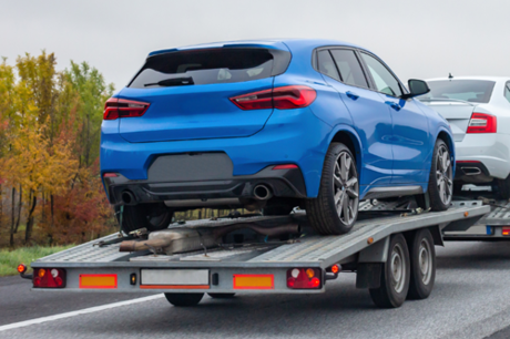 Blue car loaded on an open car trailer being transported.
