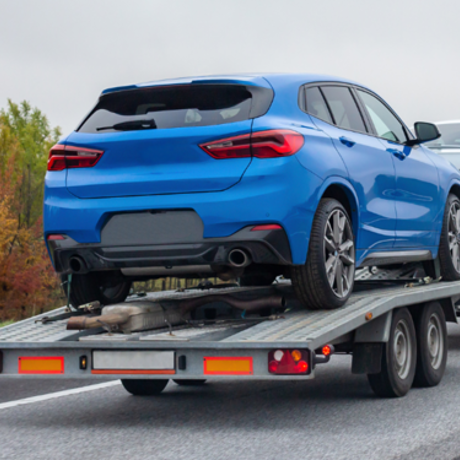 Blue car loaded on an open car trailer being transported.
