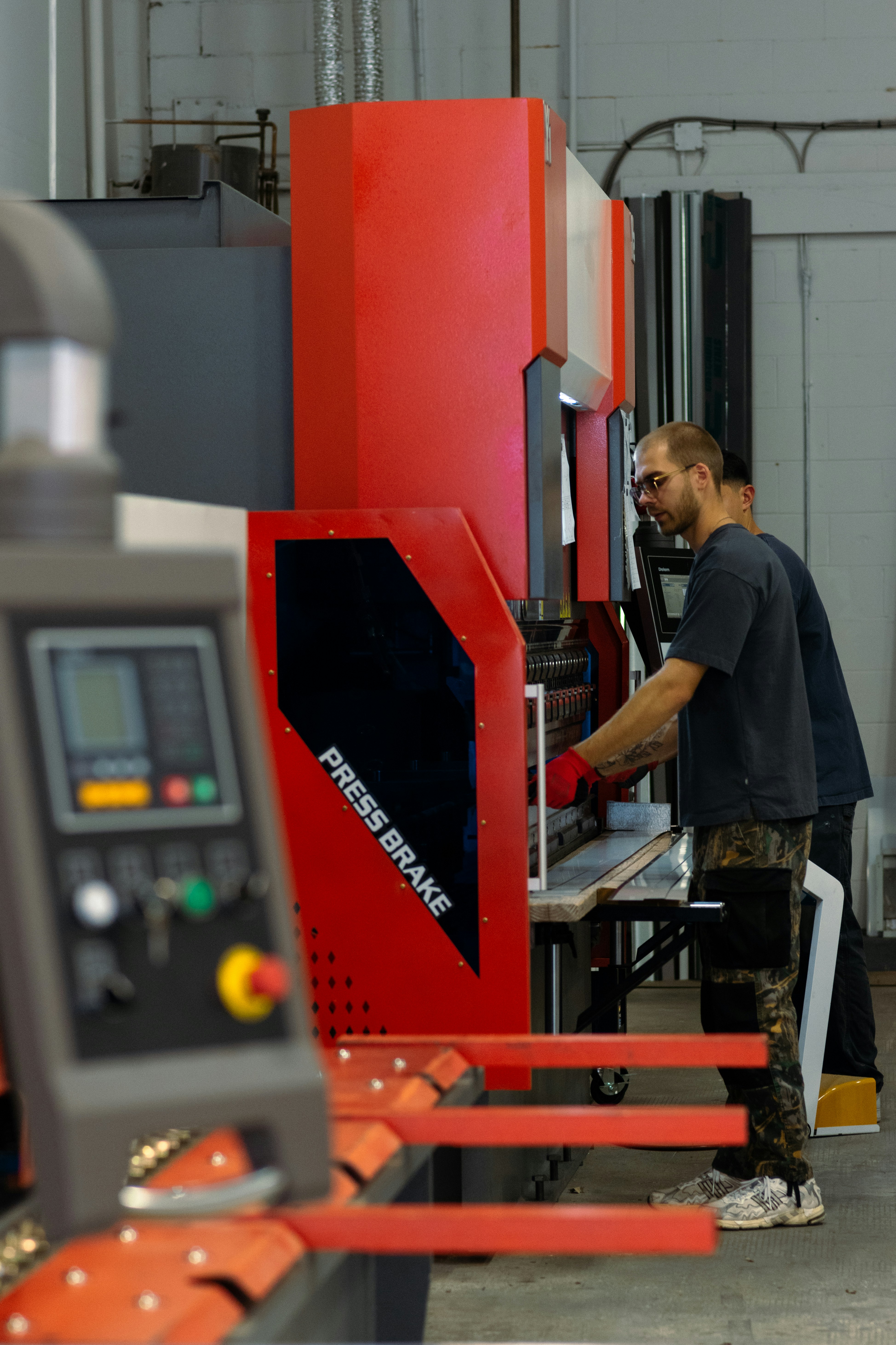 A red hydraulic press being used by two workers in a manufacturing facility.