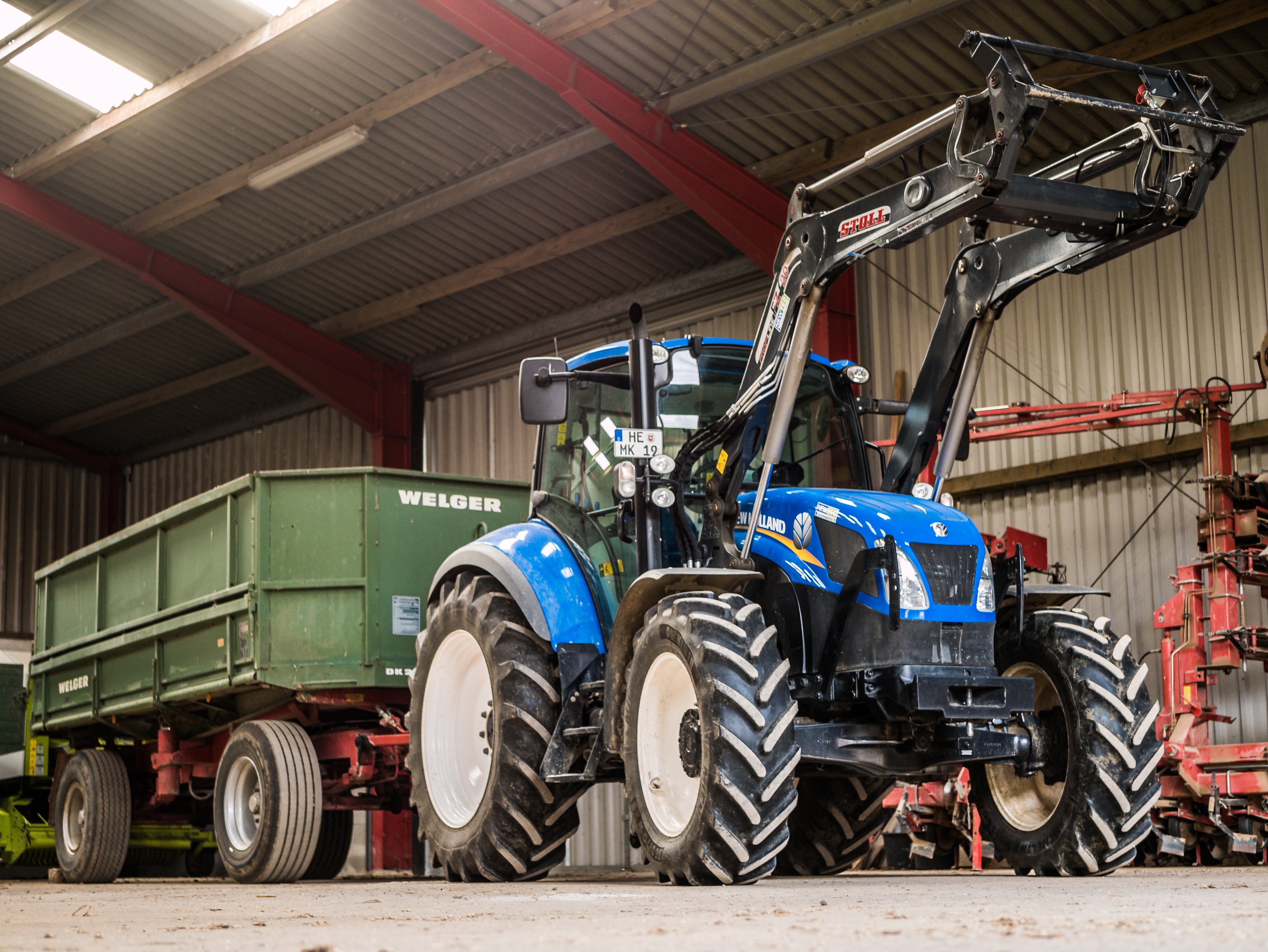 A blue utility loader tractor attached to a green trailer parked in a farmyard setting.