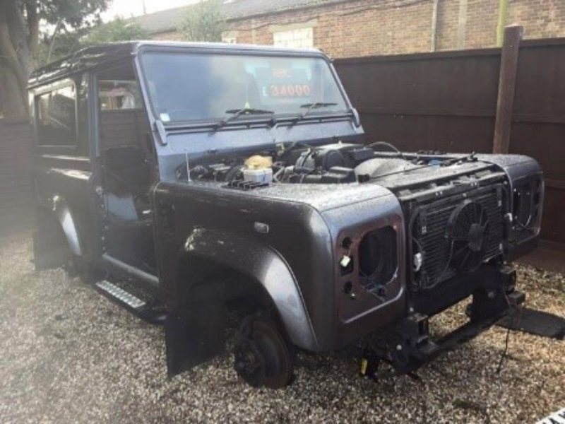 Damaged black Land Rover lacking wheels and significant bodywork components.