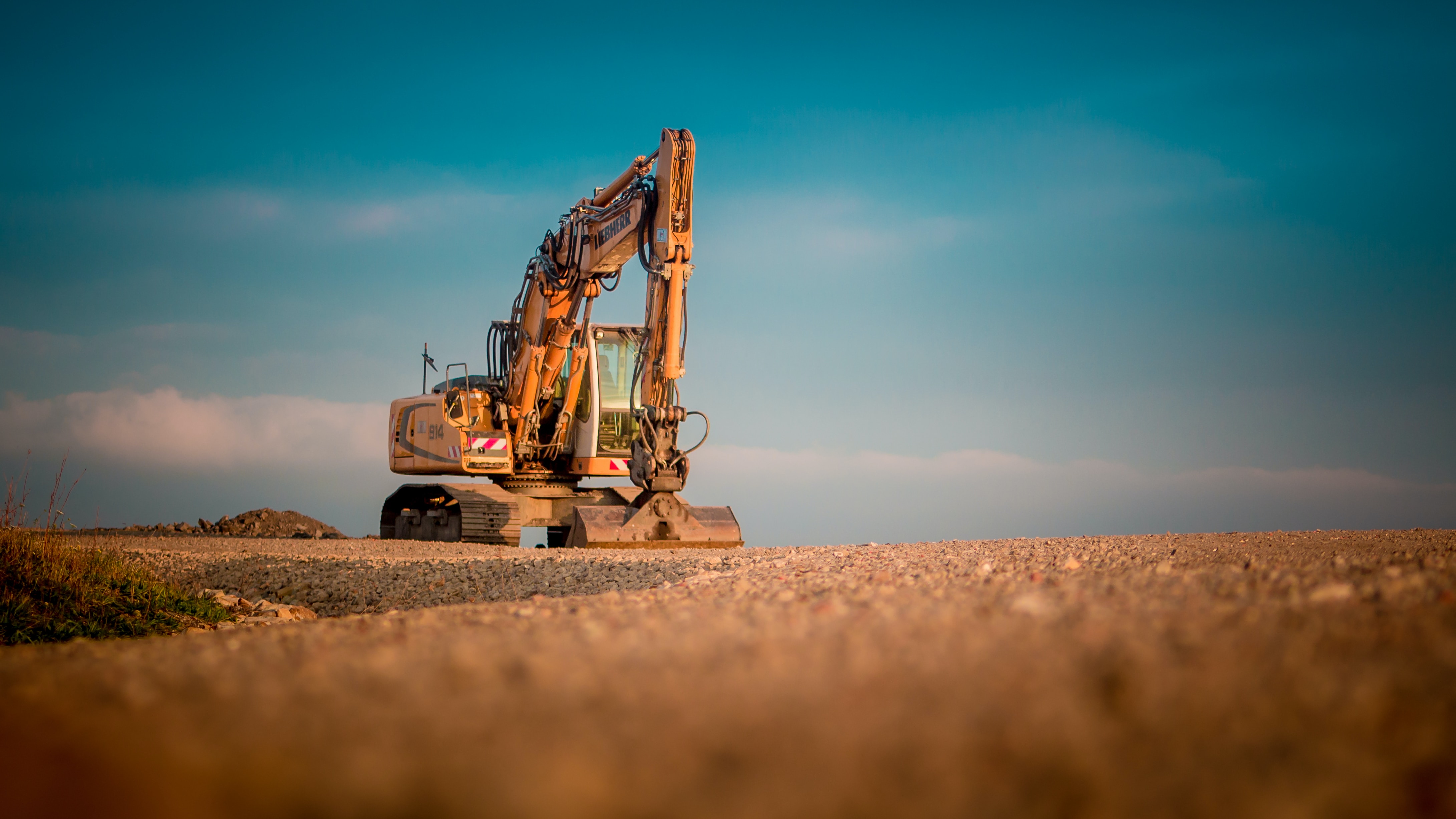 Heavy-duty yellow excavator stationed on a gravel pit with a bright blue sky overhead.
