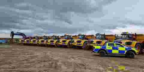 A police car parked to the right of a line of yellow off-road dumpers on a construction site.