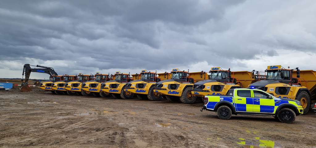 A police car parked to the right of a line of yellow off-road dumpers on a construction site.