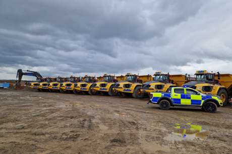 A police car parked to the right of a line of yellow off-road dumpers on a construction site.