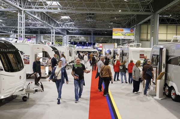 Visitors walking along a red-carpeted aisle at the Motorhome & Caravan Show, with caravans and motorhomes on either side