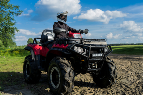 Rider stationary on a red quad bike in the countryside with green fields in the background.