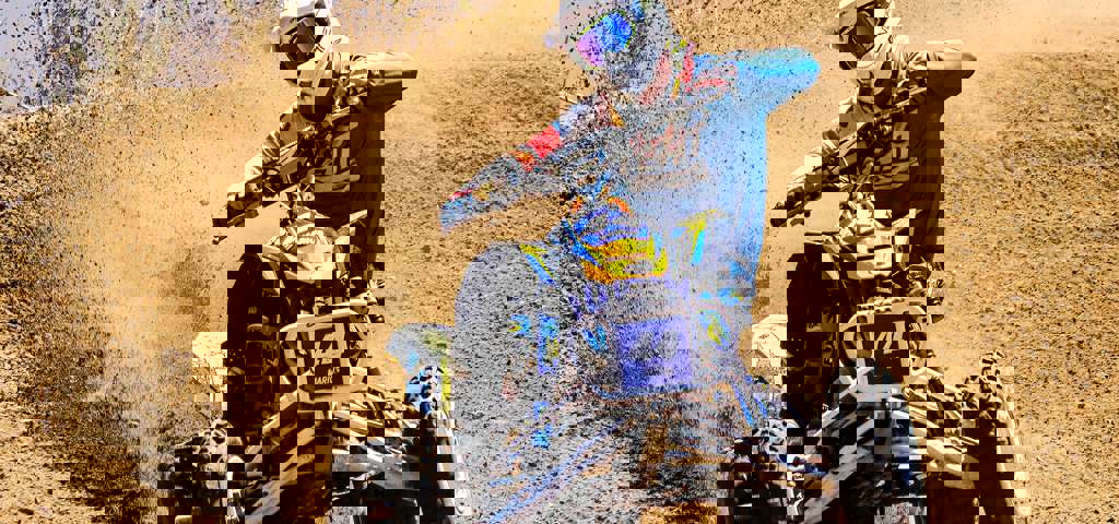 A rider on a sports ATV speeding down a sand dune, kicking up sand into the air.