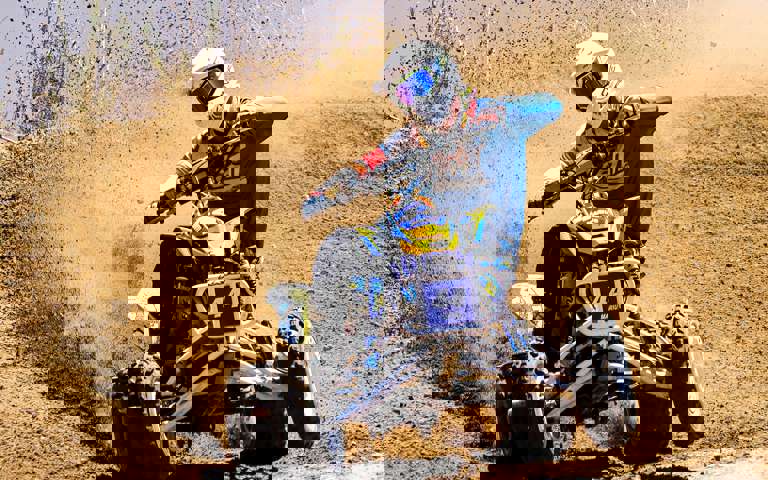 A rider on a sports ATV speeding down a sand dune, kicking up sand into the air.