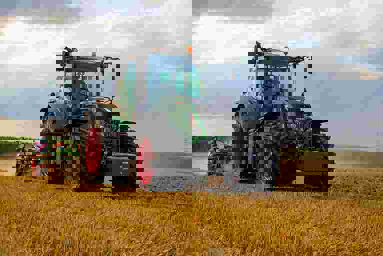 A green tractor is actively harvesting crops in a sunlit field.
