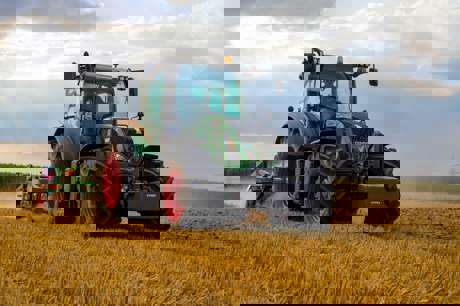 A green tractor is actively harvesting crops in a sunlit field.
