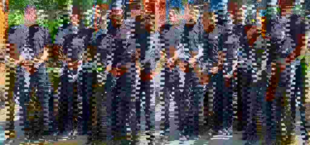 Ten Kent Police officers in blue uniforms with VIN Chip trainer, lined up in front of heavy machinery during IMI theft awareness training.