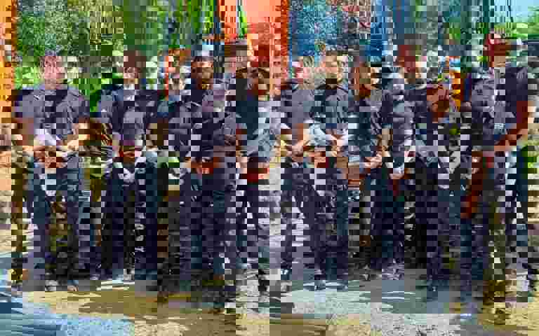 Ten Kent Police officers in blue uniforms with VIN Chip trainer, lined up in front of heavy machinery during IMI theft awareness training.
