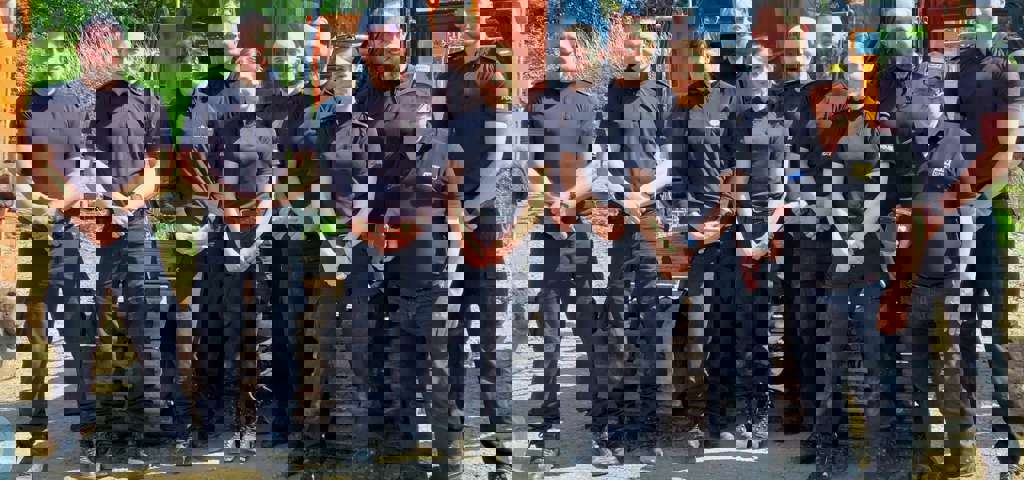 Ten Kent Police officers in blue uniforms with VIN Chip trainer, lined up in front of heavy machinery during IMI theft awareness training.