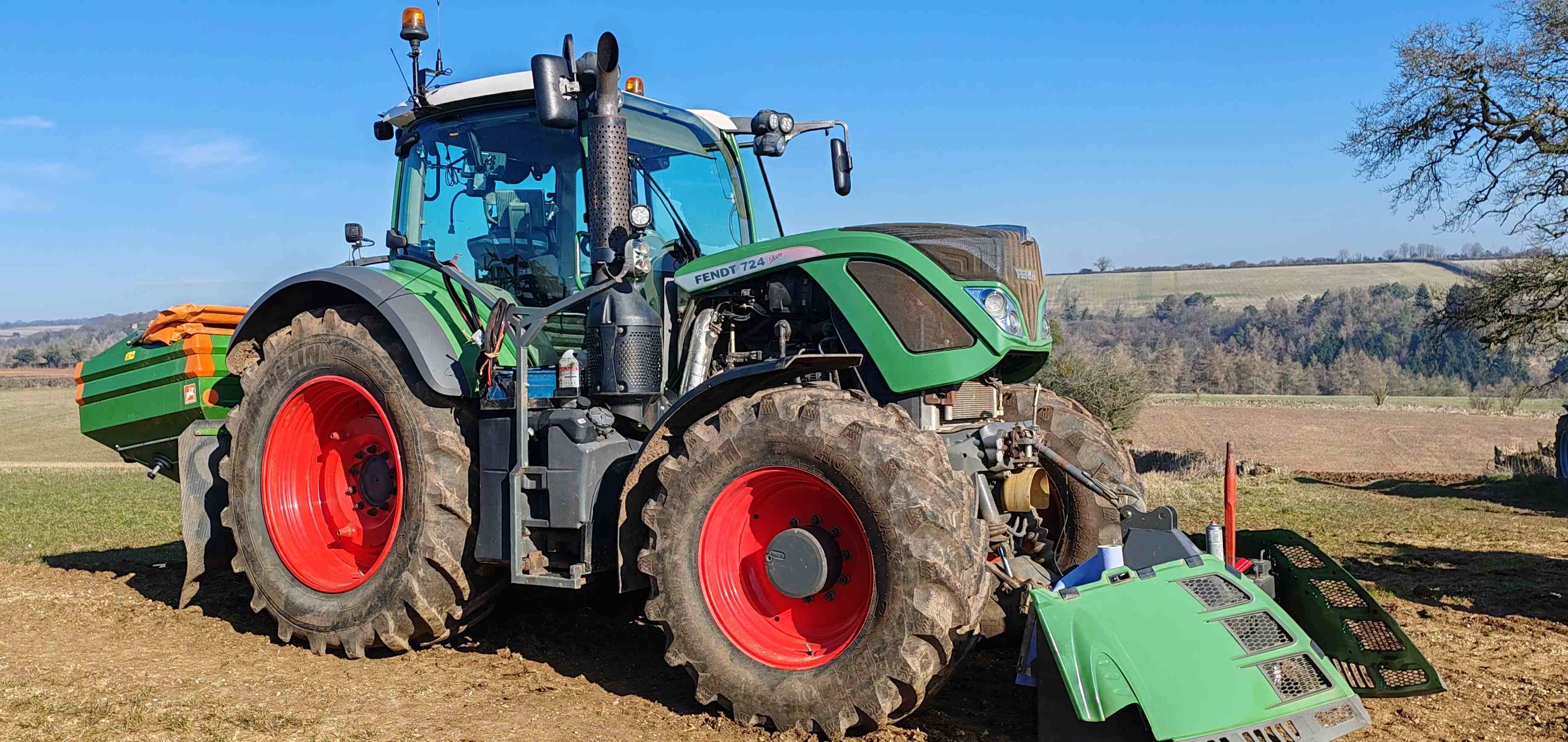A Fendt 724 Vario tractor parked on a field under a clear blue sky.