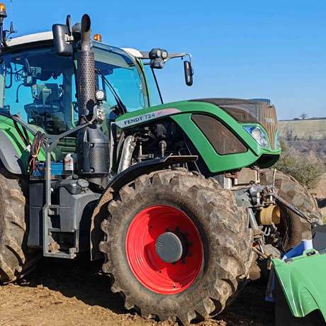 A Fendt 724 Vario tractor parked on a field under a clear blue sky.