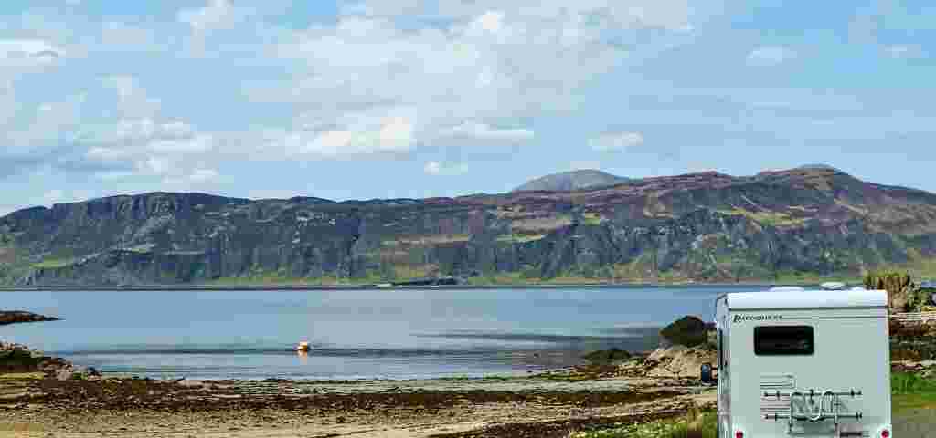 Motorhome parked beside a tranquil lake in a scenic setting.