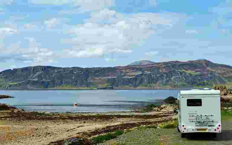 Motorhome parked beside a tranquil lake in a scenic setting.