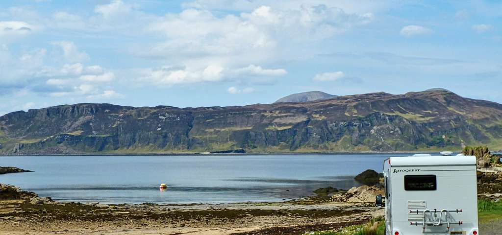 Motorhome parked beside a tranquil lake in a scenic setting.