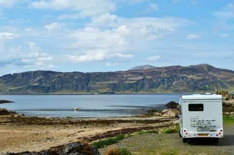 Motorhome parked beside a tranquil lake in a scenic setting.