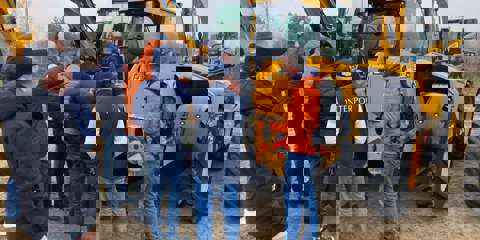 A group of students engaged in training, with JCBs and a rural landscape in the background.