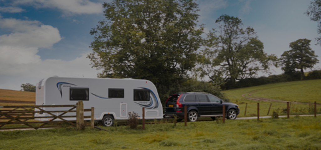 A black car towing a white caravan along a scenic route in vibrant green countryside.