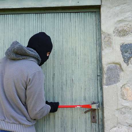 A balaclava-clad burglar is attempting to force entry into a storage facility.