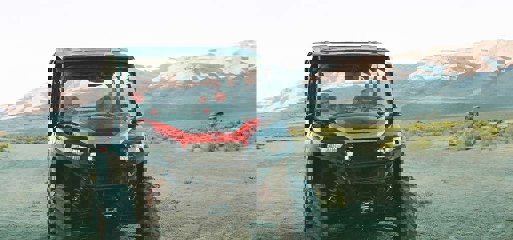 A red and black side-by-side vehicle parked in a dry landscape with sunlit mountain peaks in the distance.