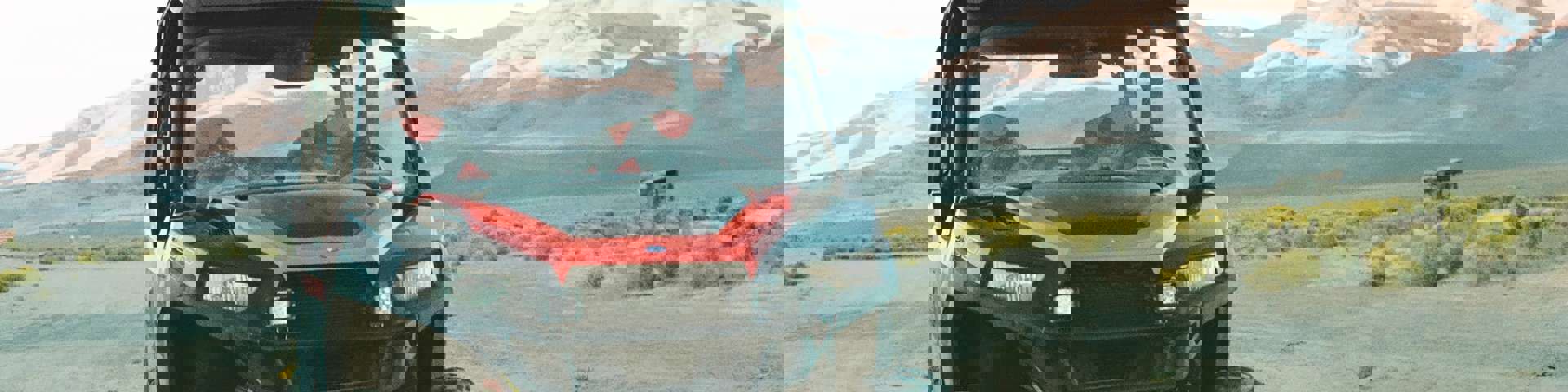 A red and black side-by-side vehicle parked in a dry landscape with sunlit mountain peaks in the distance.