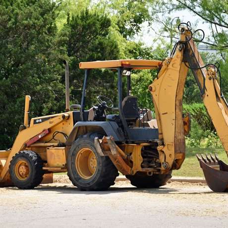 A yellow excavator positioned beside a dirt pile, set against a backdrop of green grass and trees.